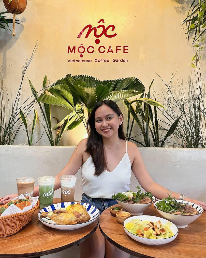 Guest with full menu spread in front of MỘC Cafe garden wall